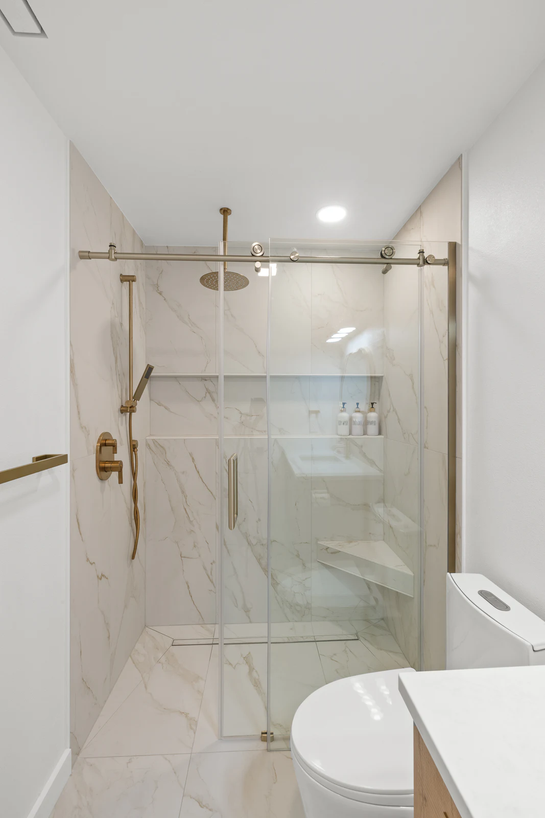 Glass shower with marble-look tile and brass fixtures